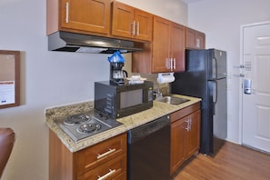 A compact kitchen with wooden cabinets, a stainless steel stove, a microwave, a dishwasher, and a black refrigerator.