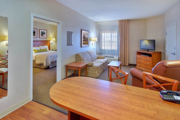 A hotel room with a bed, a sofa, a TV, a desk, and a dining table.