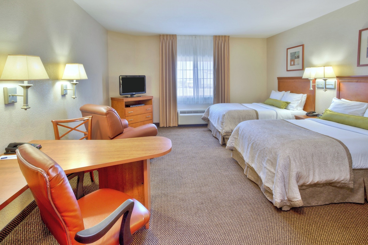 A hotel room with a desk, two beds, a TV, and a chair.