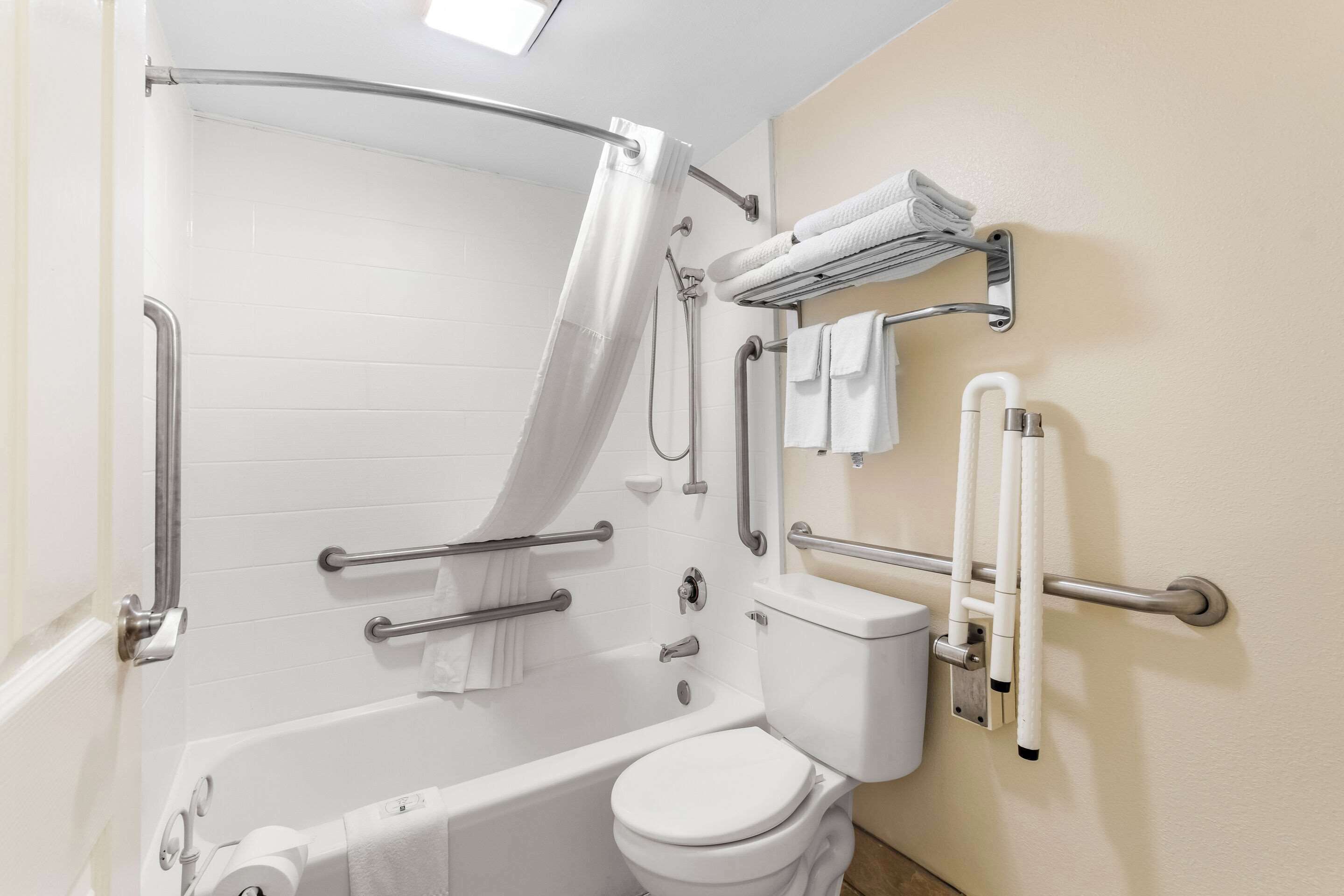A bathroom with a bathtub, toilet, and shower curtain. It includes grab bars and a towel rack.
