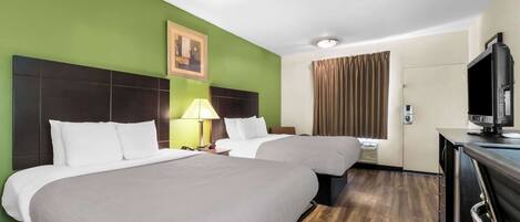 A hotel room with two beds, a television, a desk, and a window with curtains.