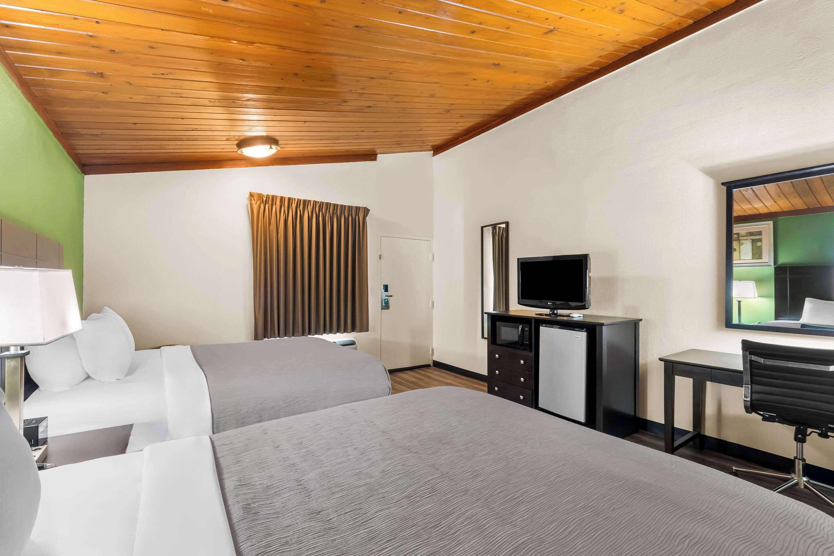 A hotel room with two beds, a desk with a computer, a television, and a mirror.