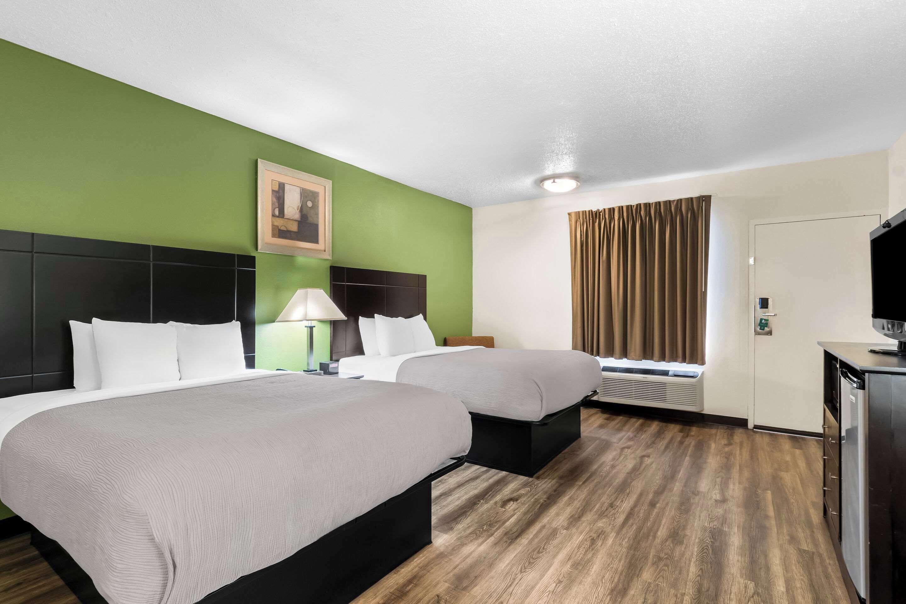 Habitación de hotel con dos camas, un escritorio, un televisor y una ventana con cortinas.