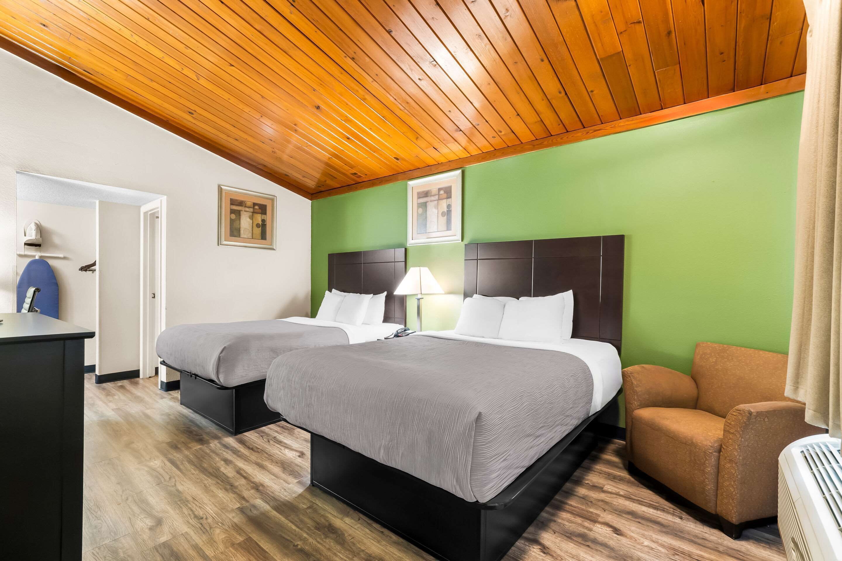 Habitación de hotel con dos camas, un escritorio, una silla y un techo con vigas de madera.