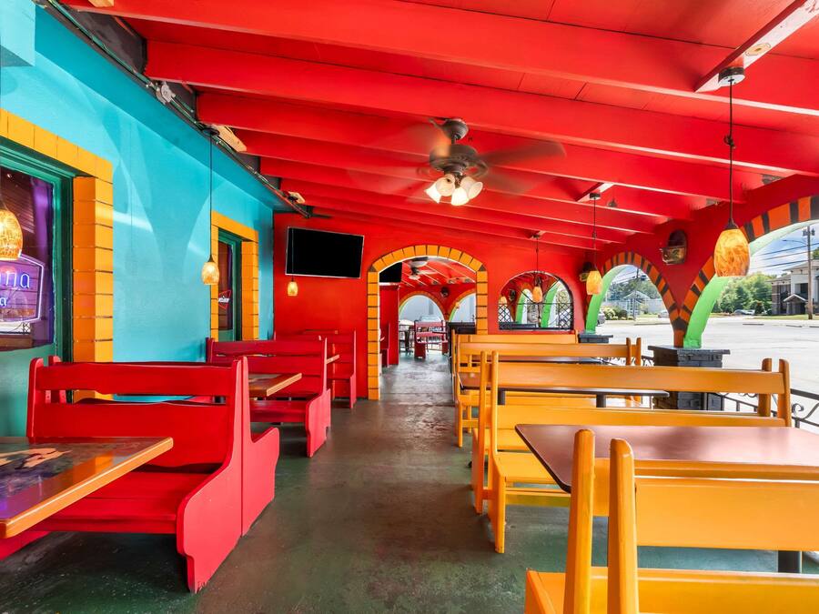 A restaurant with red and yellow seating, a ceiling fan, and a neon sign.