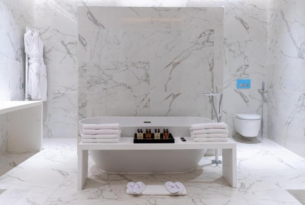 A modern bathroom with a freestanding bathtub, marble walls, a white vanity, and neatly arranged towels and toiletries.