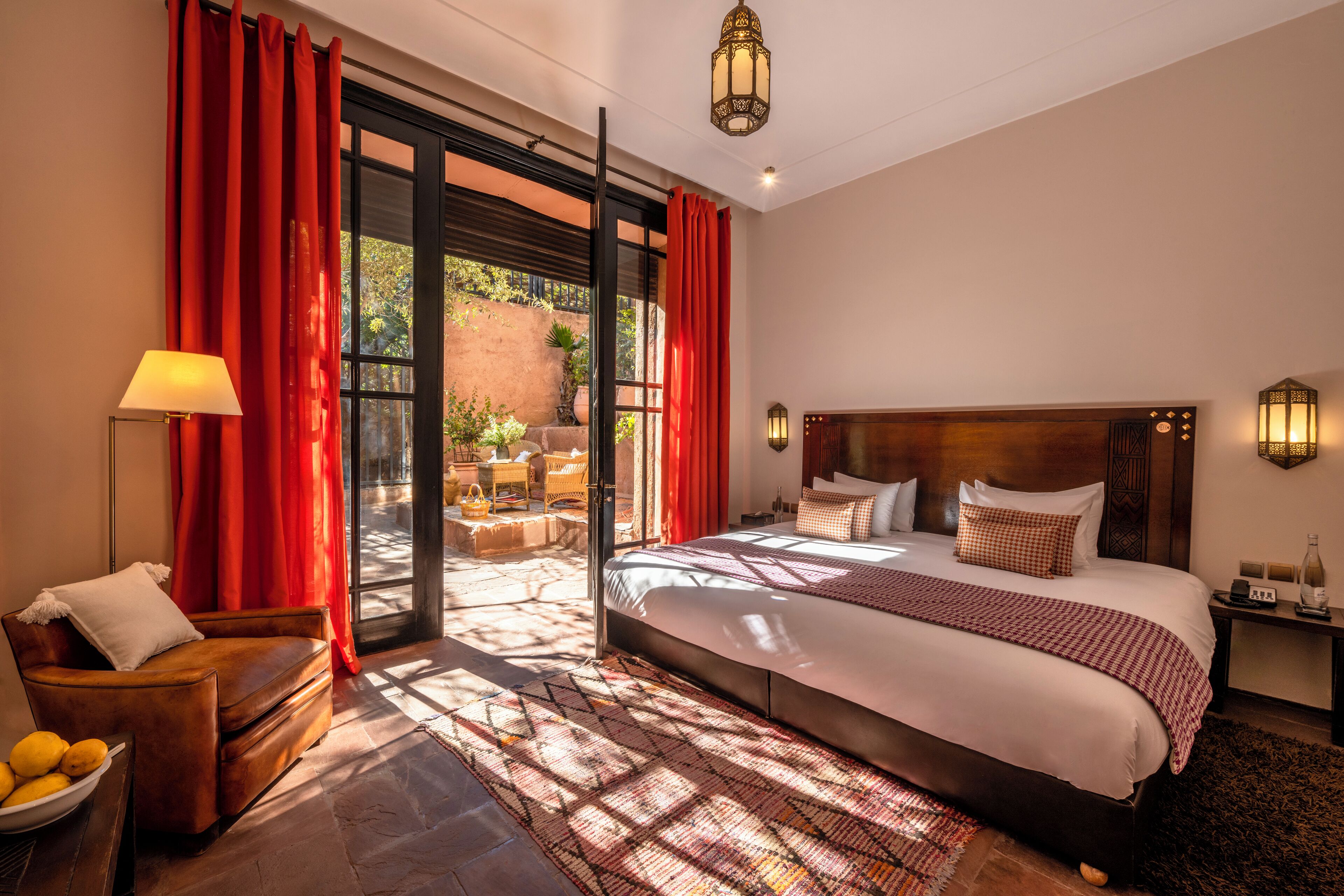 A spacious bedroom with a large bed, a wooden headboard, a nightstand, a lamp, and a view of the outdoors through a sliding glass door.
