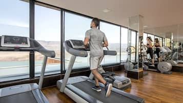 A gym with treadmills, exercise equipment, and large windows offering a view of a body of water and landscape.