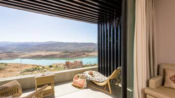 A balcony with wicker furniture, a table with drinks, and a view of a lake and mountains.