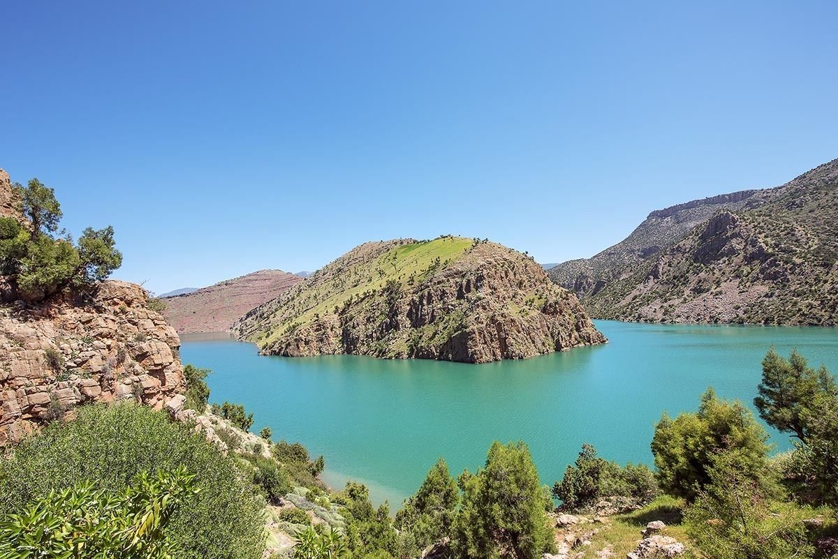 A mountainous landscape with a turquoise lake surrounded by rocky terrain and sparse vegetation.