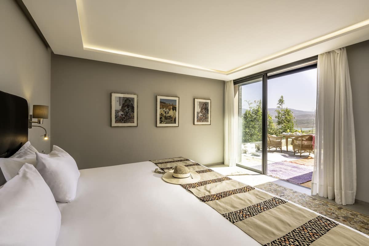 Habitación de hotel con una cama grande, vistas al exterior y un balcón con mobiliario.