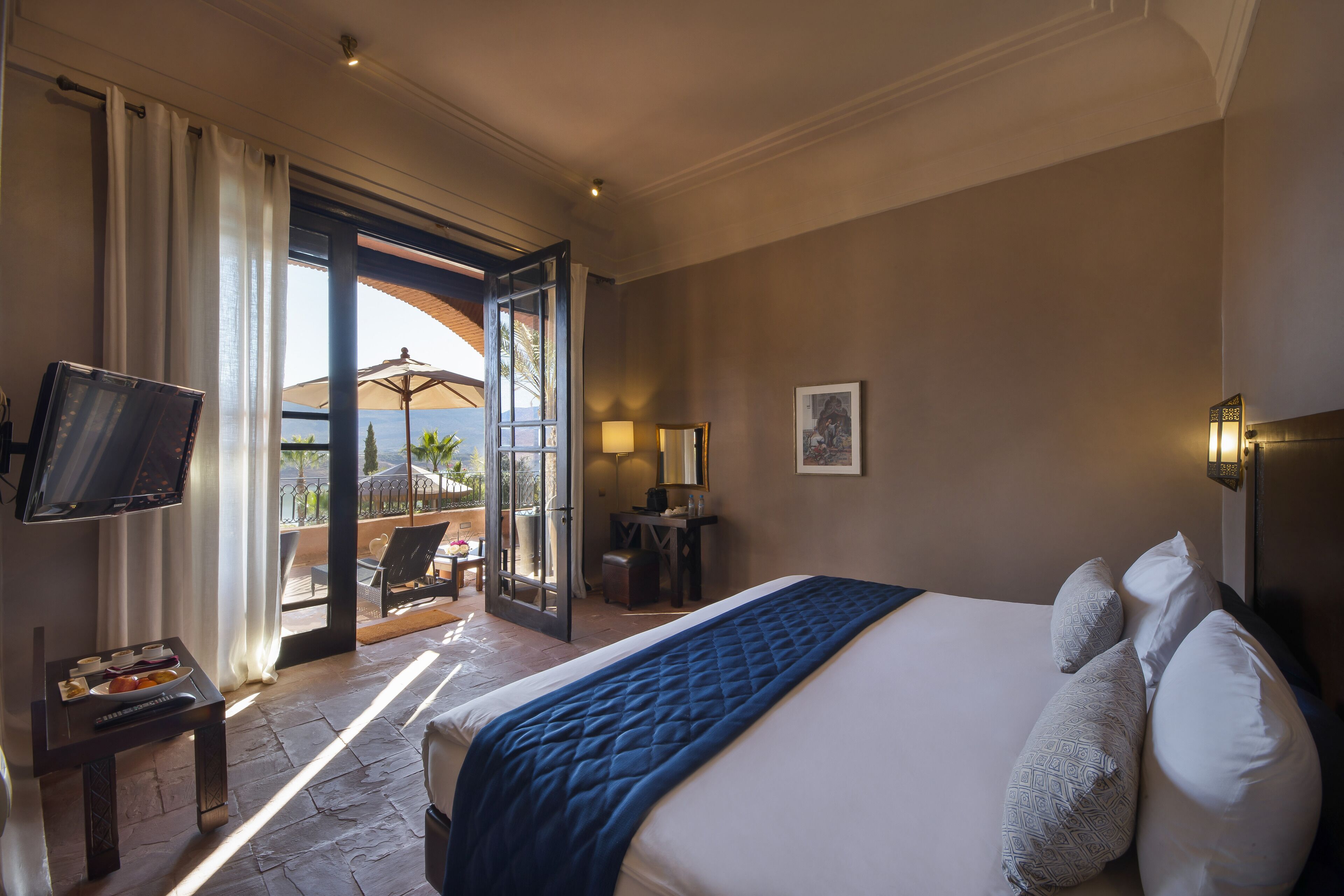 Une chambre d’hôtel avec un grand lit, une télévision, un bureau et un balcon équipé d’un parasol.