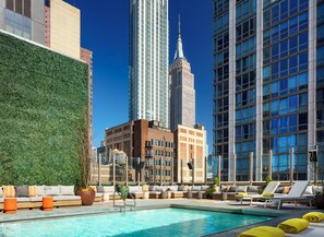 Een dakterras met een zwembad, ligbedden, een groene wand en uitzicht op de Empire State Building.