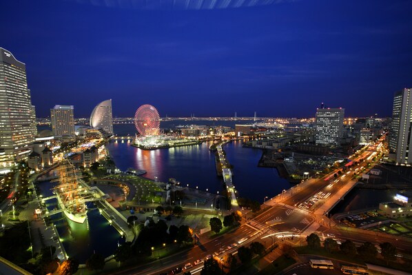 A nighttime cityscape with a prominent Ferris wheel and a large ship, surrounded by illuminated buildings and a busy waterfront.