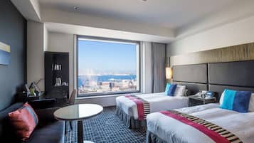 A hotel room with two beds, a sofa, a small table, a TV, and a large window with a city view.