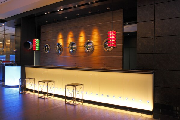 Un área de bar moderna con una pared de madera, espejos circulares y taburetes iluminados.
