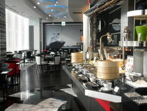 A modern restaurant interior with a buffet setup, dining tables, and chairs.