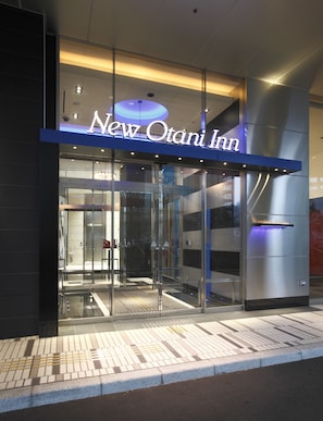 Esterno del New Otani Inn con ingresso in vetro, insegne illuminate e un design architettonico moderno.