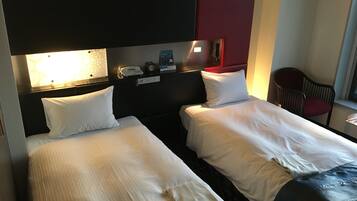 A hotel room with two beds, a desk with a lamp, a chair, and a red accent wall.