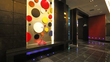 A modern lobby with a geometric wall design, a red sculpture, and a tiled floor.