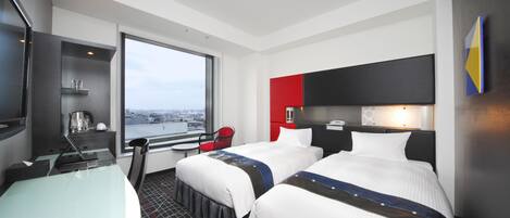 A hotel room with two beds, a desk, a chair, a TV, and a window with a city view.