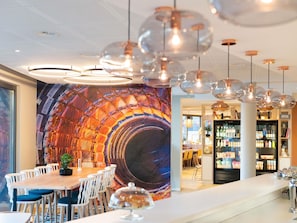 A restaurant with a large mural, hanging pendant lights, and a bar area. - ibis Geneve Petit Lancy (Lancy)