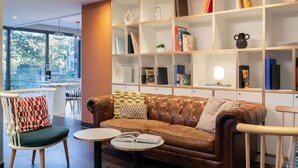 A modern living area with a leather sofa, a round table, and a bookshelf. - ibis Geneve Petit Lancy (Lancy)