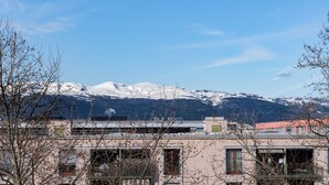 Área residencial com edifícios, céu claro e montanhas cobertas de neve ao fundo.
