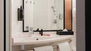 Uma casa de banho moderna com uma pia branca, um espelho, um porta-toalhas e uma zona de duche.