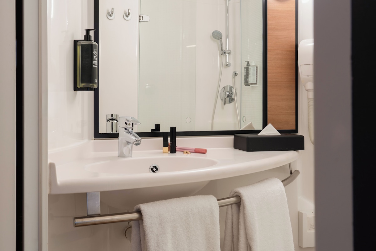 A modern bathroom with a white sink, a mirror, a towel rack, and a shower area.