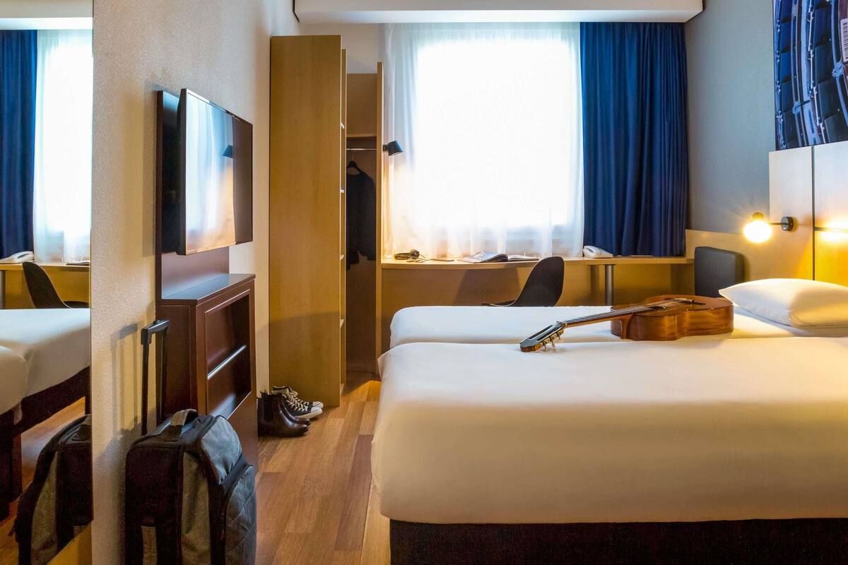 A hotel room with a bed, a guitar, a TV, a desk, and a wardrobe.