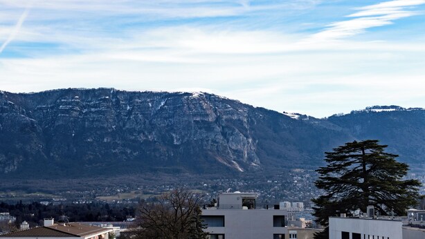 Paisagem montanhosa com um edifício de telhado plano e uma grande árvore em primeiro plano.
