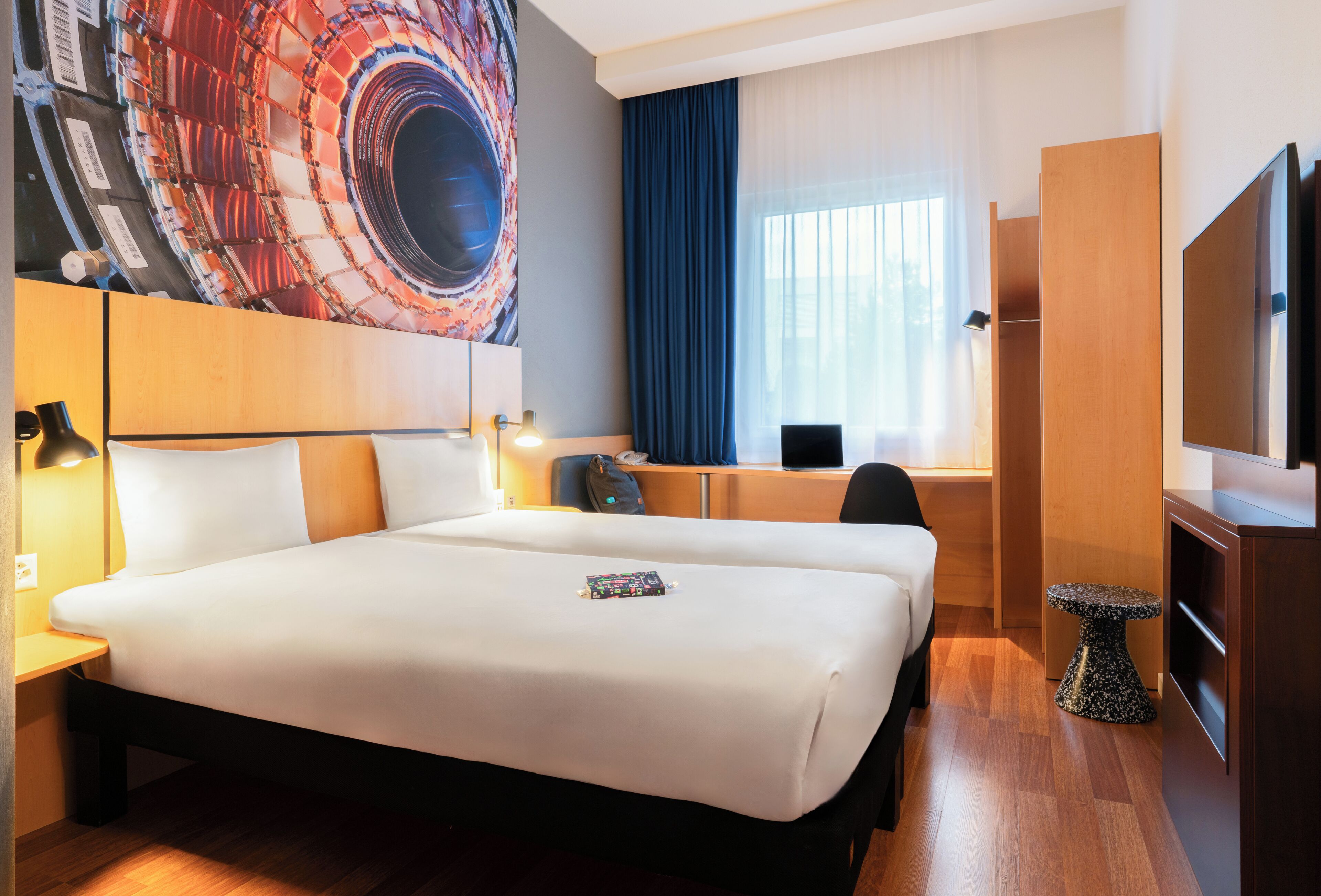 Ein Hotelzimmer mit einem großen Bett, einem Schreibtisch mit Computer, einem Fernseher und einem Gemälde an der Wand.