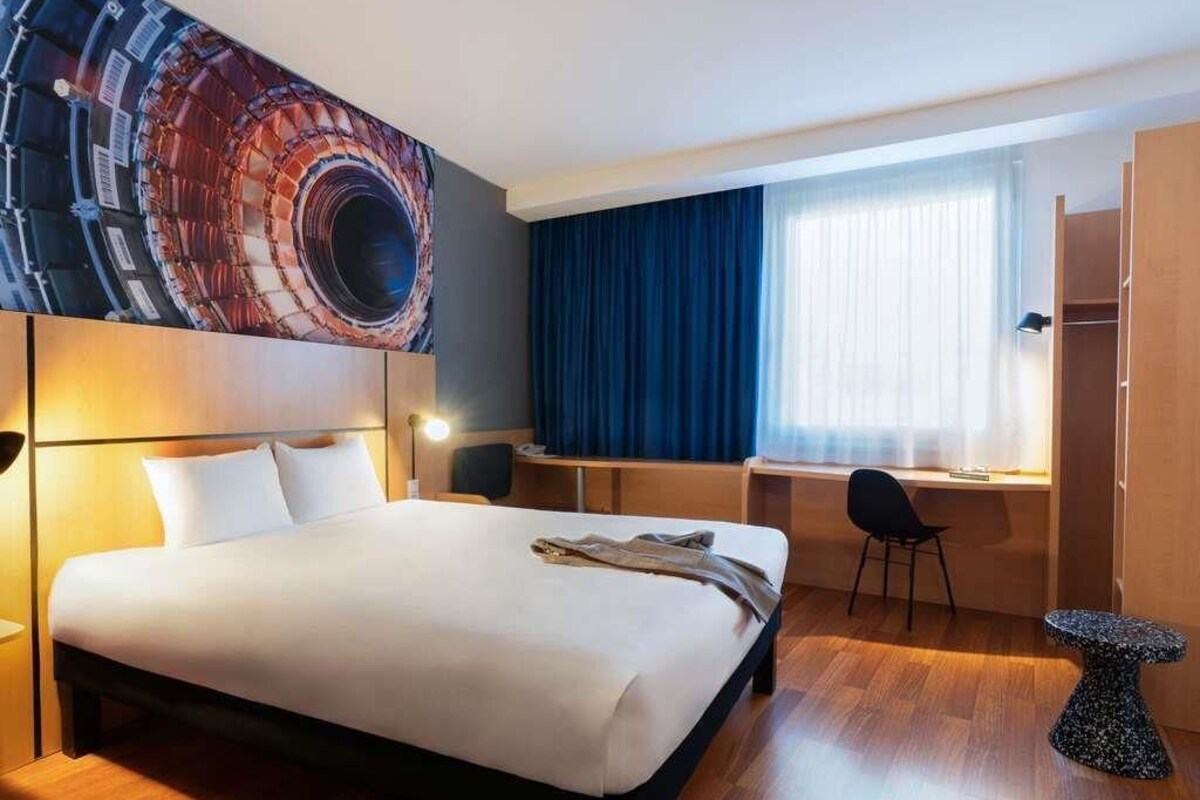A hotel room with a bed, desk, chair, and a small table.