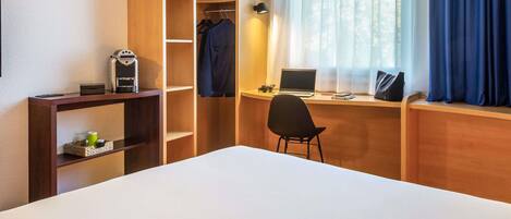Una habitación de hotel con cama, escritorio con computadora portátil, silla, estantería y ventana con cortinas.
