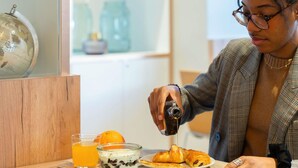 A person pouring syrup onto a croissant, a glass of orange juice, and a bowl of yogurt with fruit on a wooden table. - ibis Geneve Petit Lancy (Lancy)