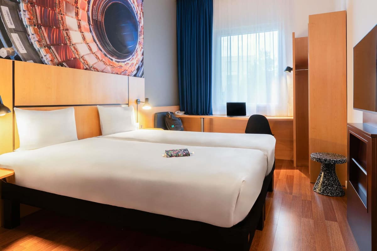 A hotel room with a large bed, a desk with a laptop, a TV, and a decorative wall piece.