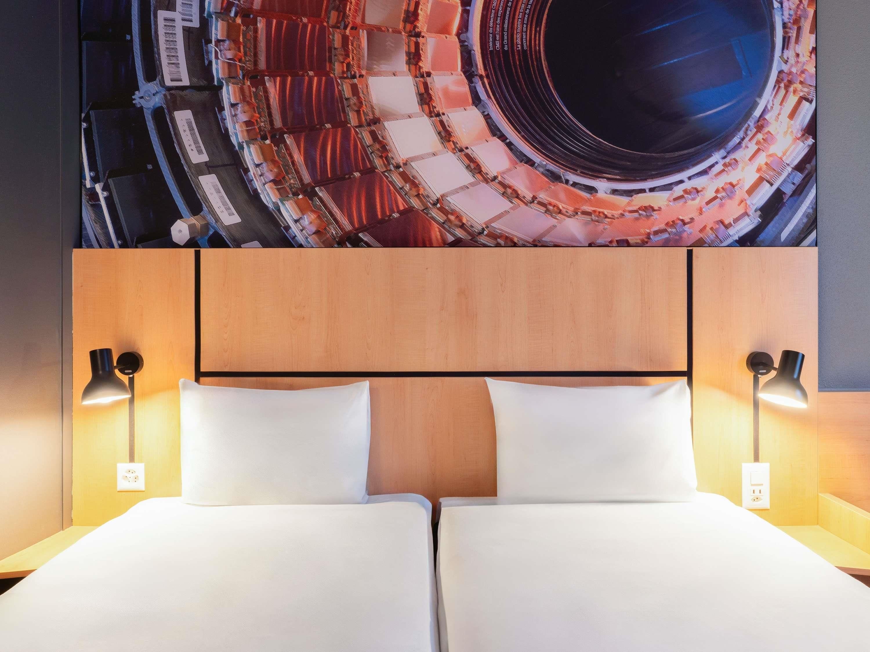 Una habitación de hotel con una cama grande, dos lámparas de noche y un mural circular único en la pared.