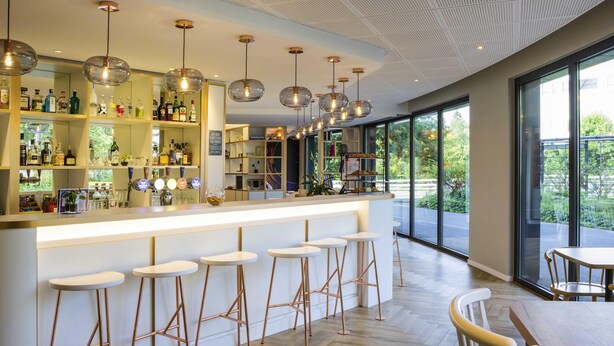 A modern bar area with a wooden herringbone floor, copper bar stools, and pendant lighting. - ibis Geneve Petit Lancy (Lancy)