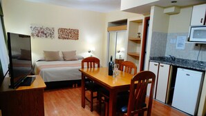 Una habitación de hotel compacta con una cama, una pequeña mesa de comedor y un kitchenette.
