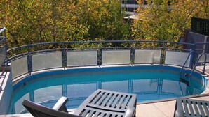 Una piscina con borde curvo, rodeada por una barandilla metálica. Dos sillas de descanso en primer plano.