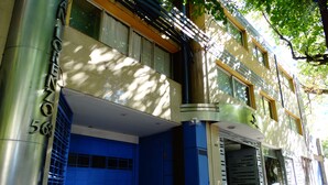 Un edificio con una puerta de garaje azul, un pilar metálico con números y un árbol que da sombra.