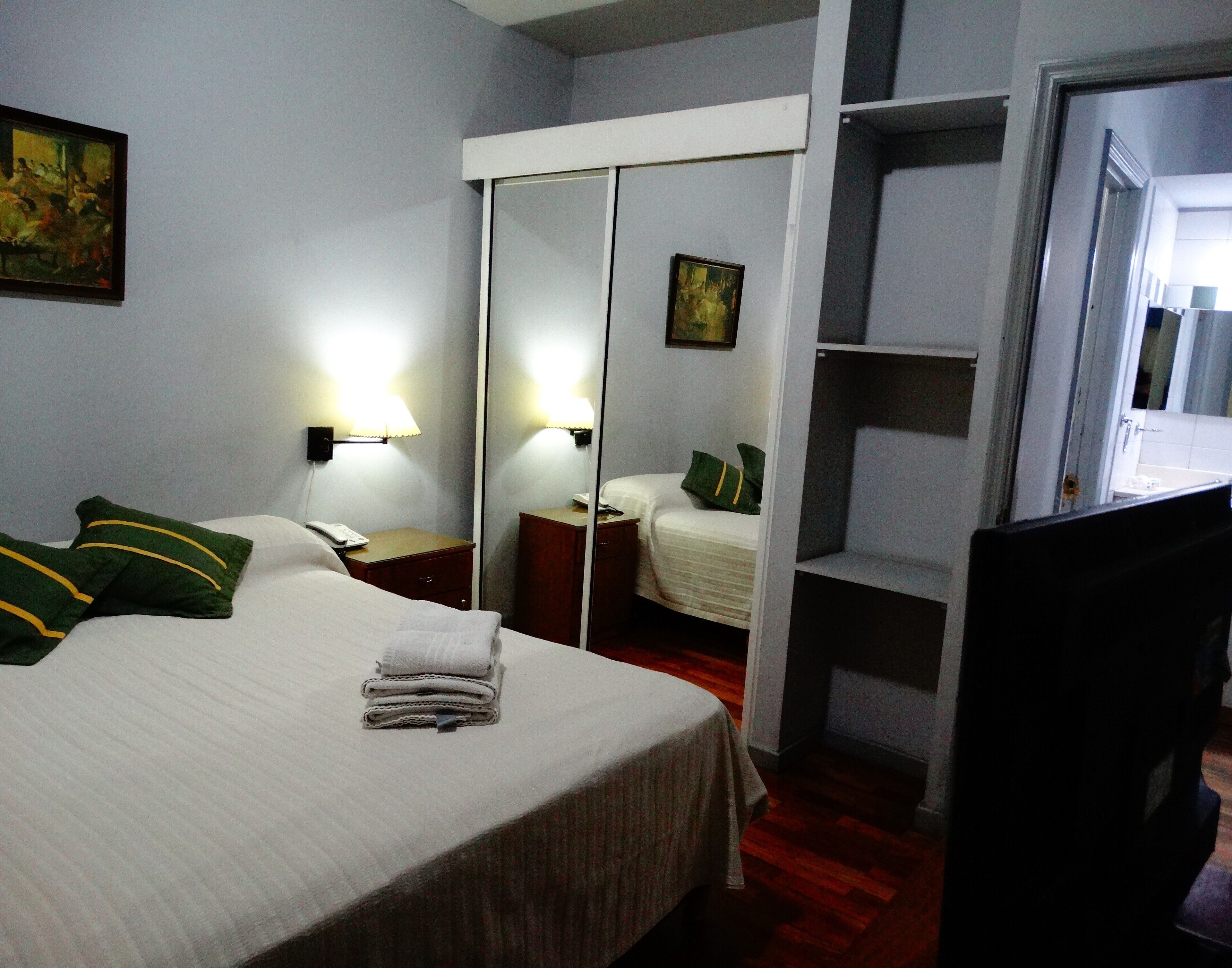 Ein Hotelzimmer mit Bett, Nachttisch, Spiegel, kleinem Schreibtisch, Stuhl und Ablagefläche.