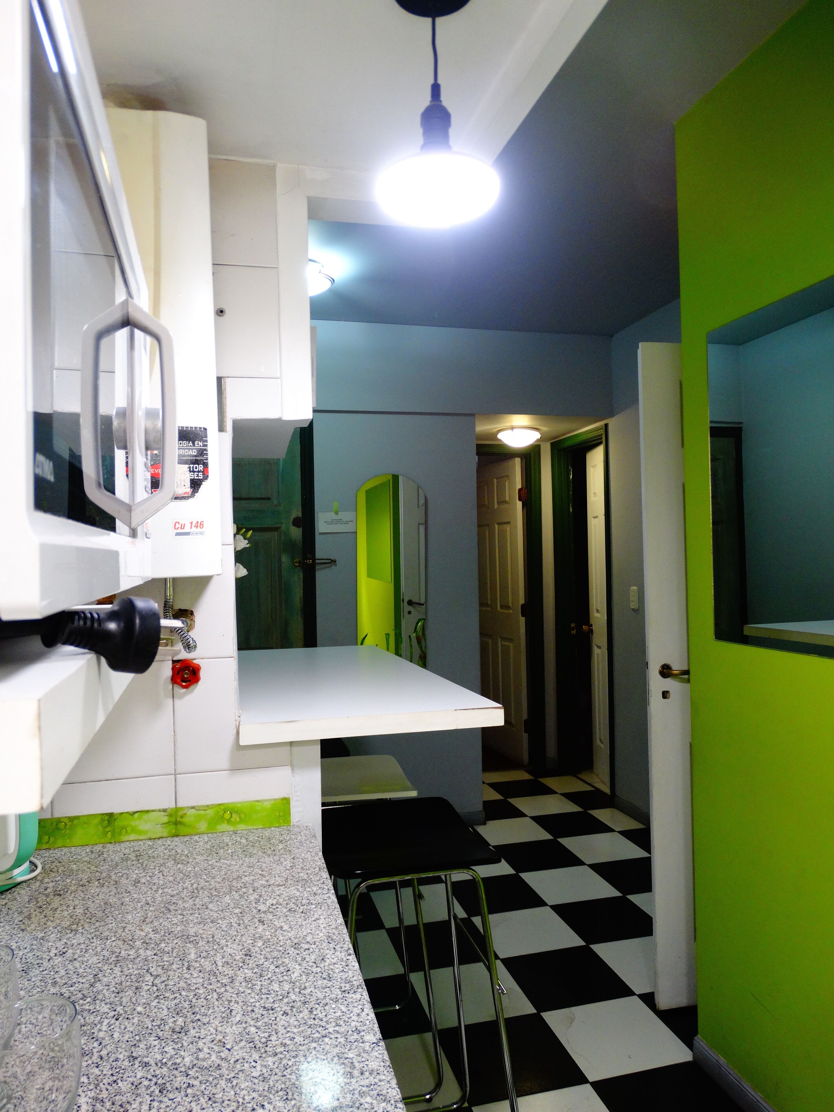 Una cocina con encimera blanca, suelo a cuadros blanco y negro, y puerta verde.