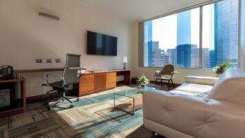 A modern office space with a large window, a flat-screen TV, a desk, office chairs, a sofa, and a coffee table.