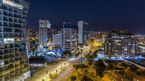 Une vue nocturne d’une ville avec des bâtiments modernes, de larges rues et des zones illuminées.