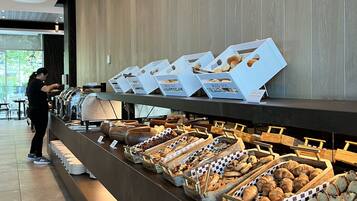 A buffet area with various food items displayed in trays and boxes, a person serving, and a sign indicating homemade pastries.