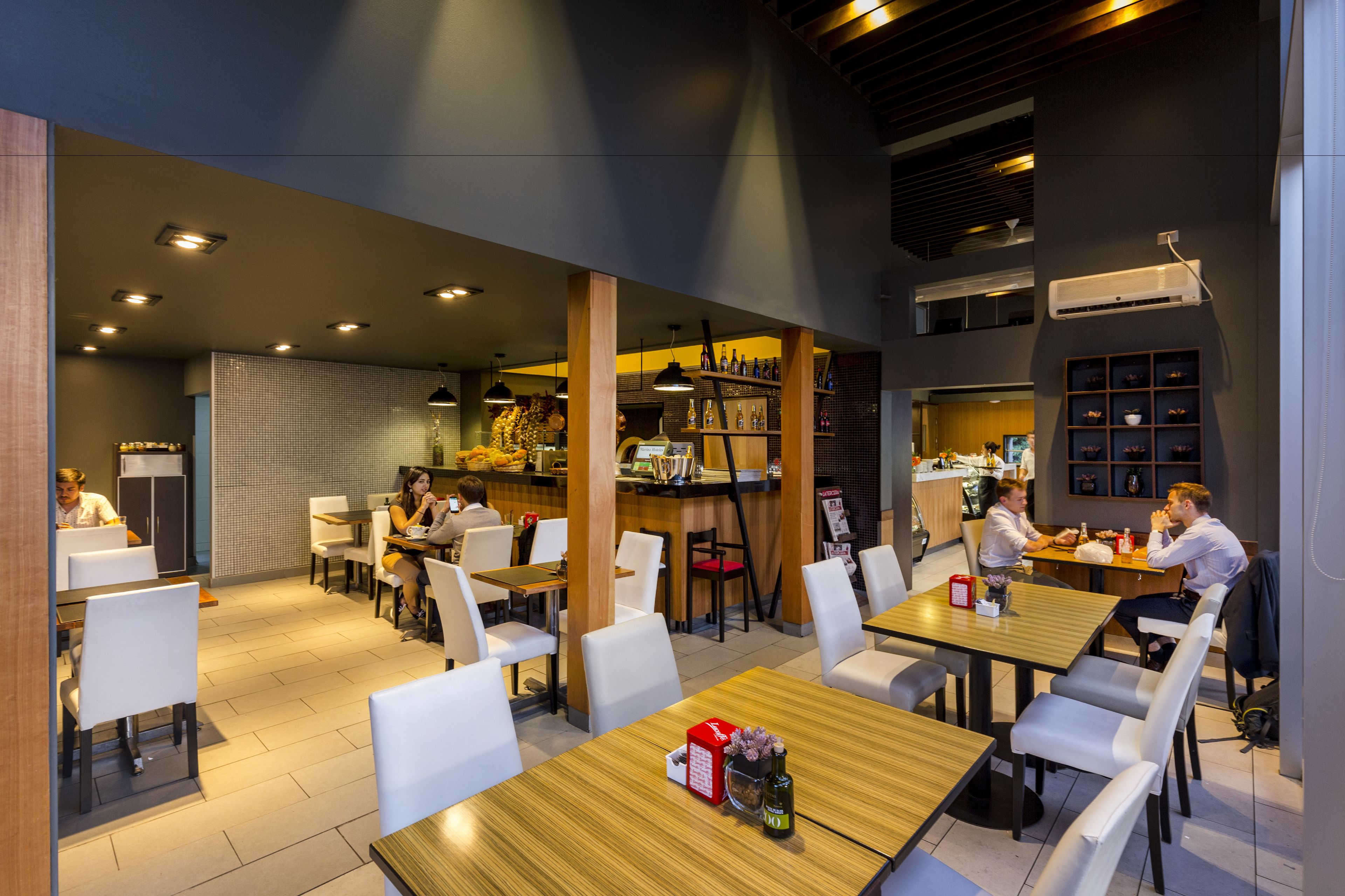 A modern restaurant with multiple dining areas, wooden tables, and white chairs.