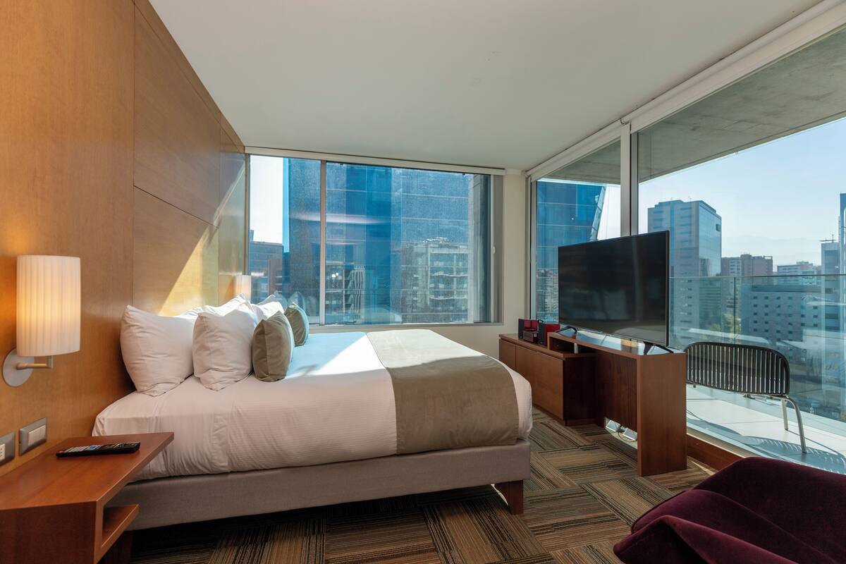 Una habitación de hotel moderna con una cama grande, televisión, escritorio y vistas a la ciudad.