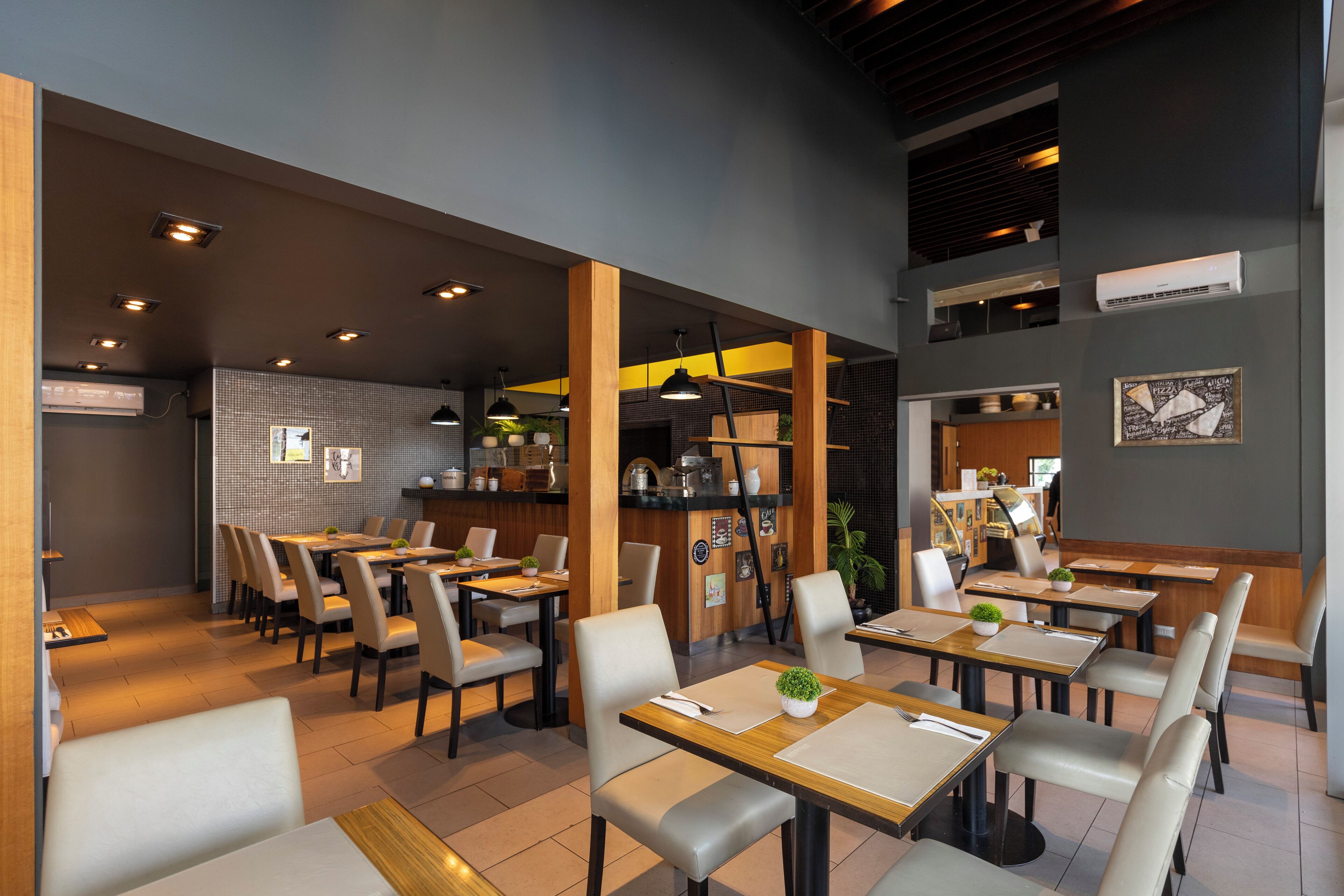 A modern restaurant with multiple dining tables and chairs, wooden beams, and a tiled backsplash.